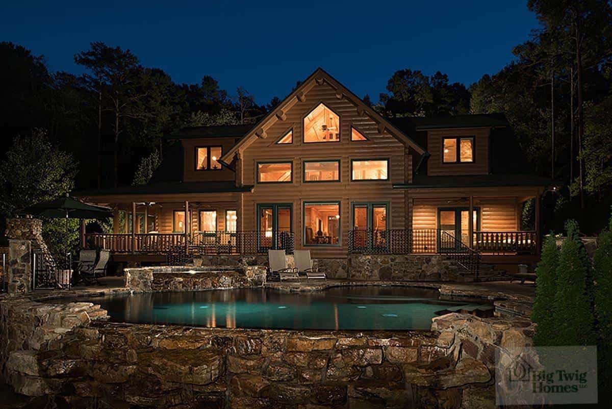 Bennett cedar log home at dusk, with illuminated windows and stone terraces